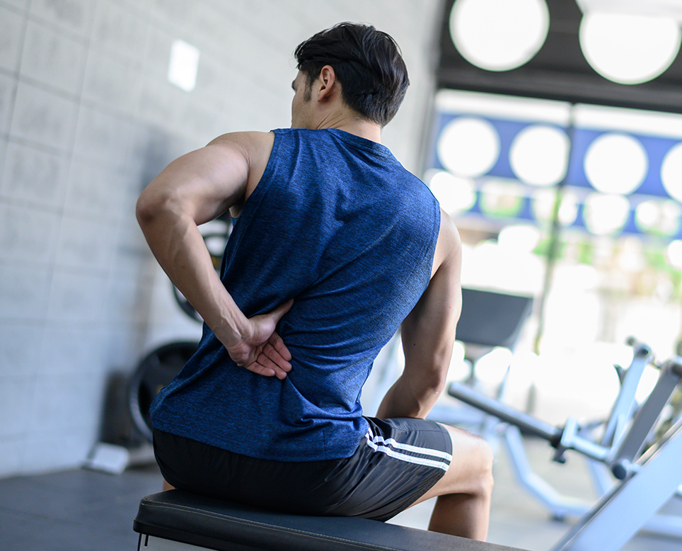 Man sitting on a gym bench, back turned, indicating back pain