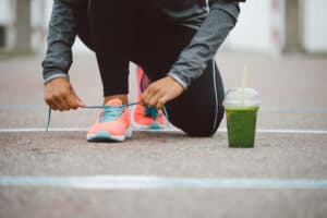 Close-up of a runner tying shoelaces on a track with a green smoothie nearby, emphasizing sports nutrition for endurance training.
