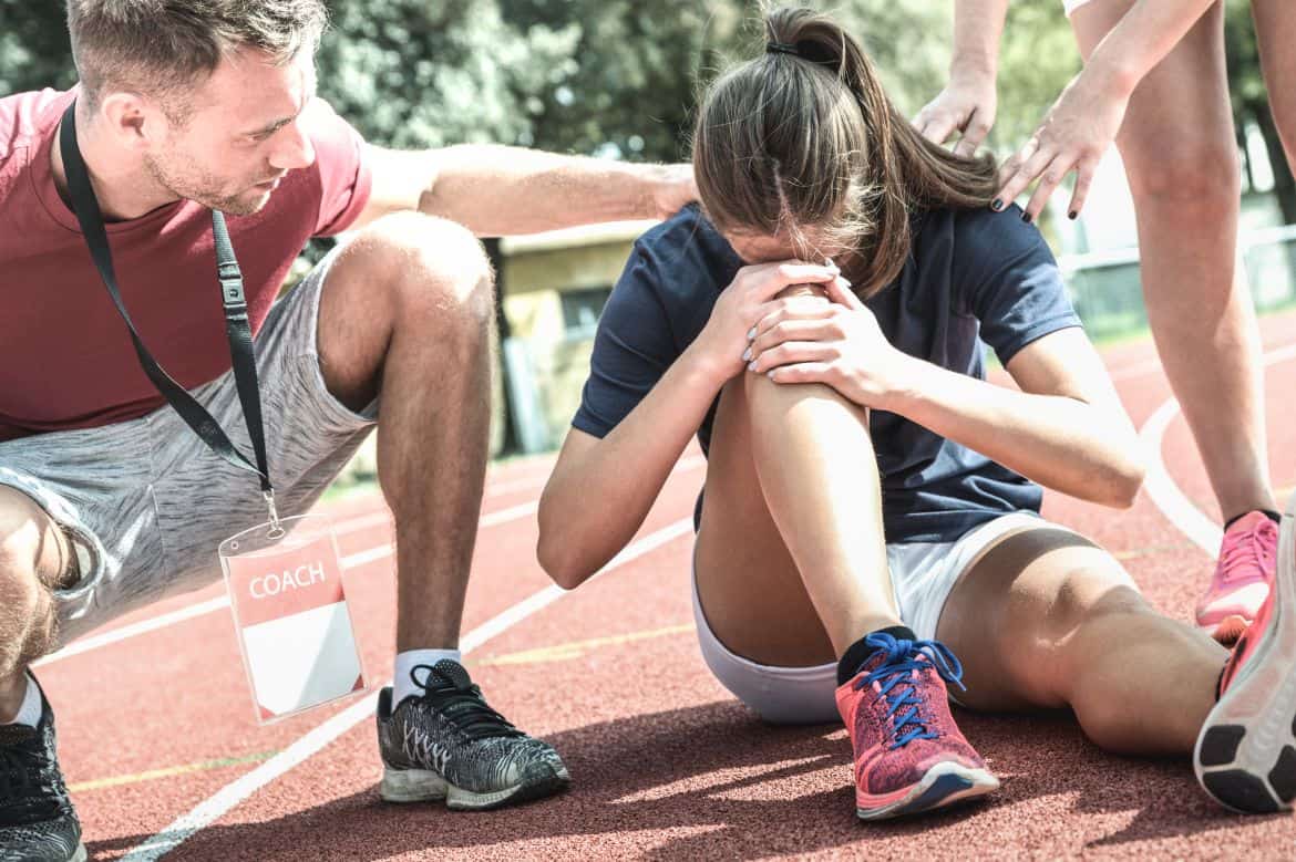 Female athlete getting injured during athletic run training - Male coach taking care on sport pupil after physical accident - Team concept with young sporty people facing mishaps casualty
