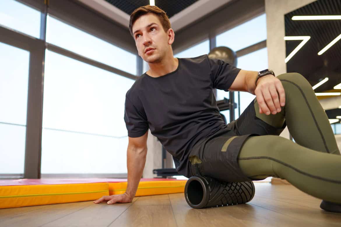 The man is massaging his leg muscles with the foam roller