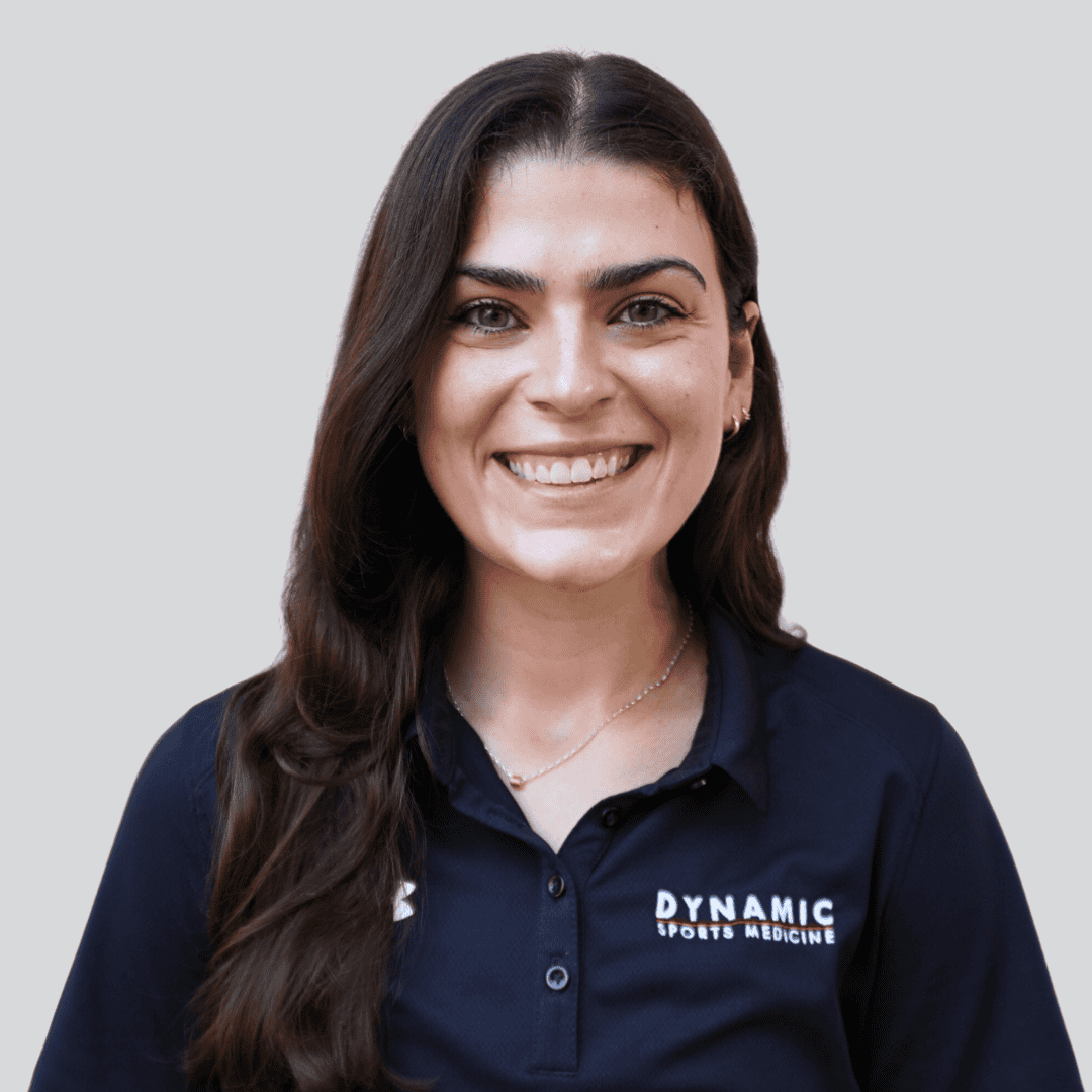 Sports medicine professional smiling in navy uniform with Dynamic Sports Medicine logo, providing expert injury treatment and physical therapy for athletes and active individuals.