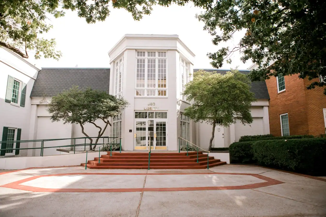 Modern medical clinic building entrance with wheelchair accessible ramp, surrounded by green trees and landscaping, offering specialized sports medicine and injury recovery services.