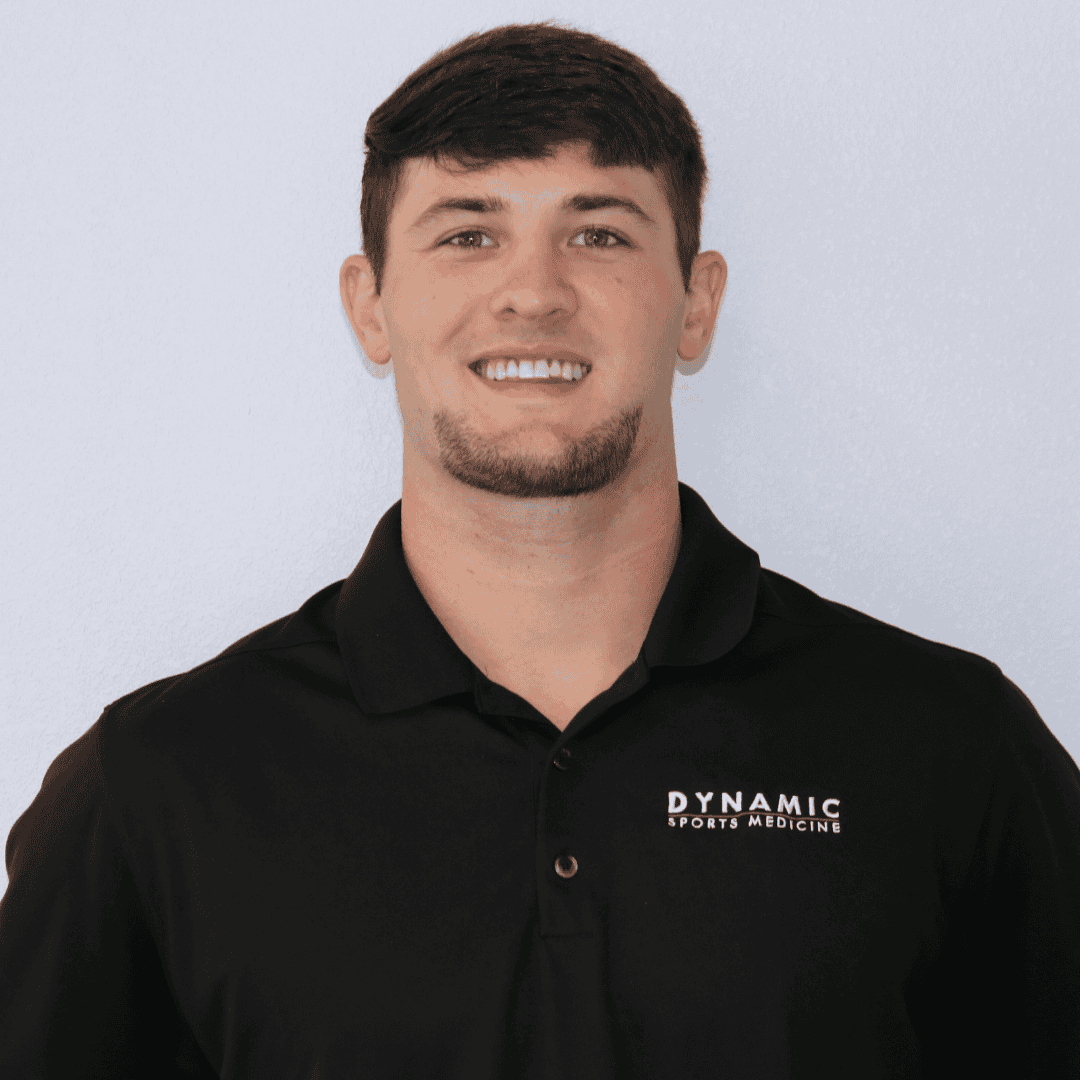 Portrait of a male sports medicine professional in a black polo shirt with "Dynamic Sports Medicine" logo, smiling confidently.
