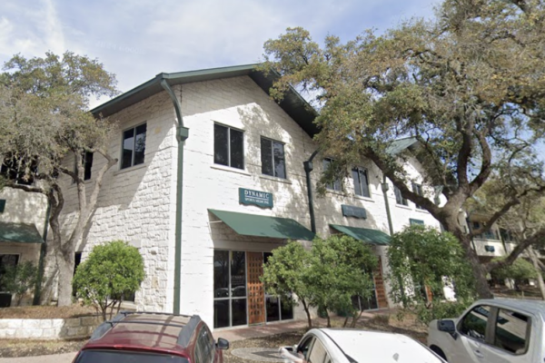 Exterior view of the Dynamic Sports Medicine clinic in Westlake Hills, showing a white building with green awnings and surrounding trees.