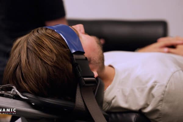 Person experiencing neck pain while sitting at a desk, highlighting the importance of ergonomic posture and sports medicine interventions for neck discomfort.