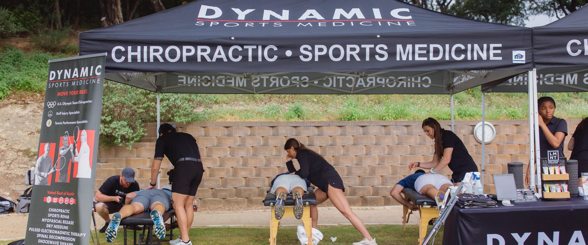 Outdoor sports medicine and chiropractic care session with therapists providing treatment to athletes under a branded tent.