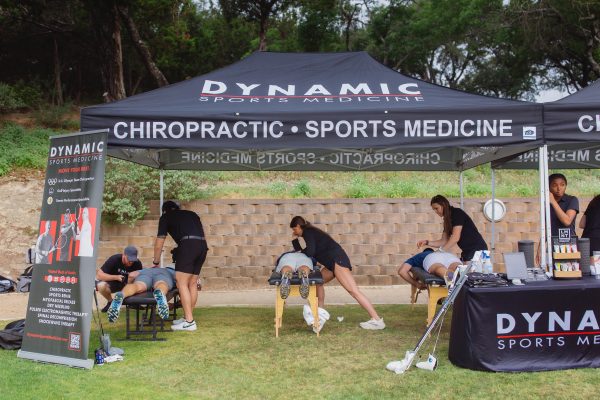 Outdoor sports medicine and chiropractic care session with therapists providing treatment to athletes under a branded tent.