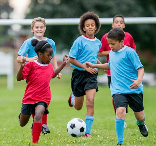 Group of children playing soccer outdoors, showcasing pediatric sports injury prevention and treatment at Dynamic Sports Medicine.