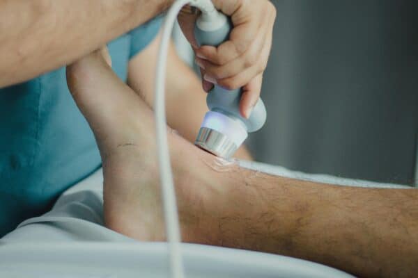 Medical professional performing ultrasound therapy on Achilles tendon for tendinopathy treatment at a sports medicine clinic.