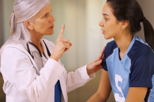 A doctor in a white coat holds up one finger to test a young female athlete's eye tracking during a sideline concussion evaluation.