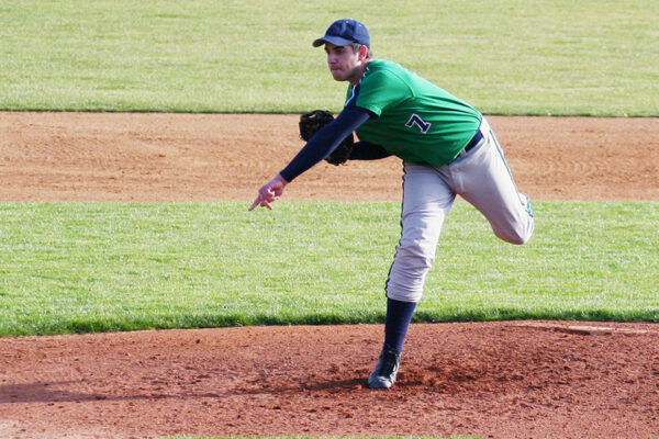 Baseball pitcher in green jersey and gray pants following through on a pitch from the mound.